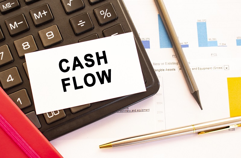 Text CASH FLOW on white card with metal pen, calculator and financial charts.